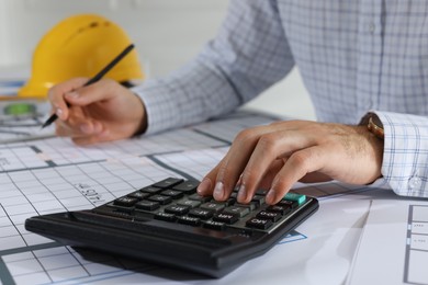 Photo of Architect working with construction drawings and calculator indoors, closeup