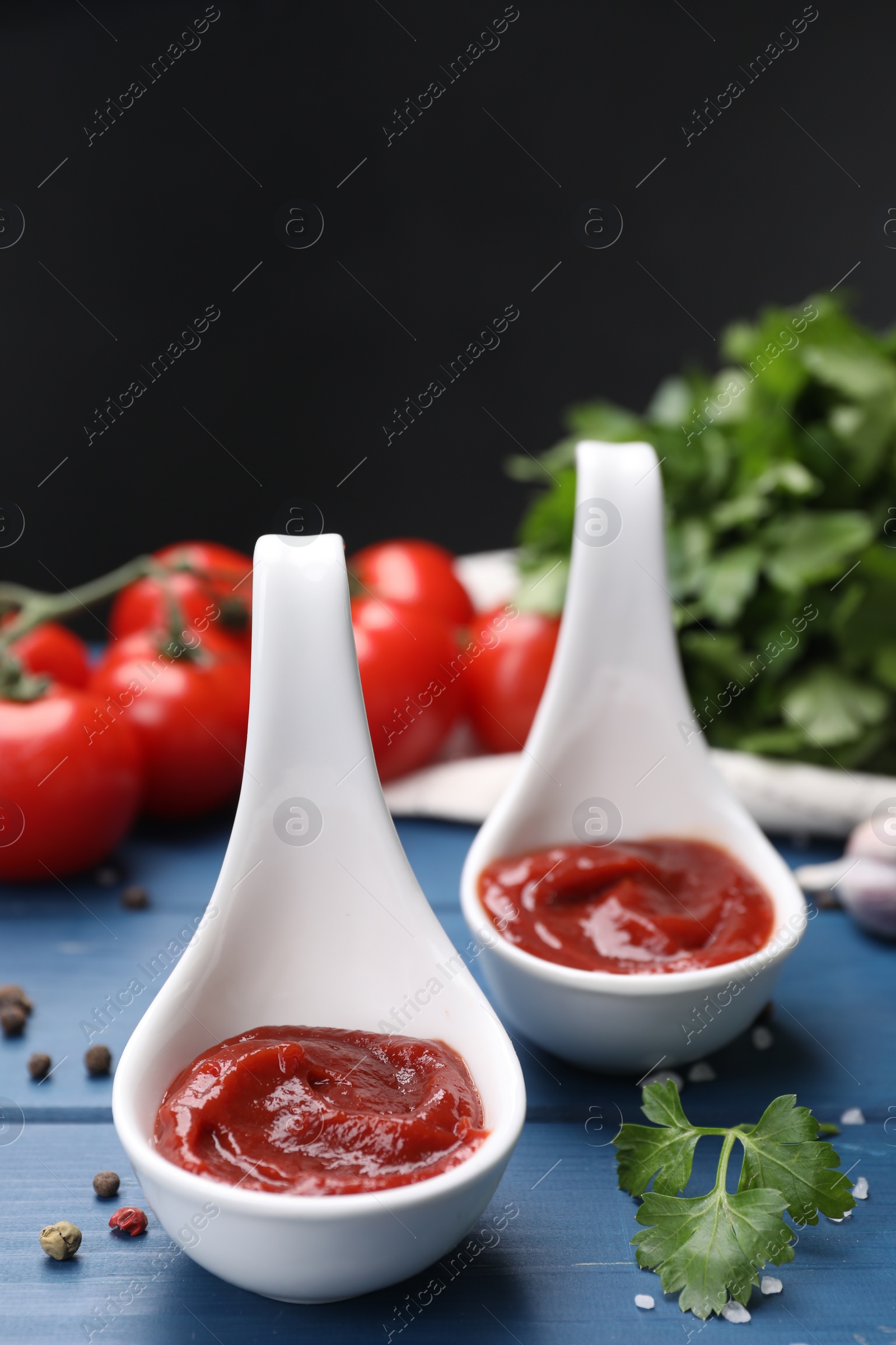 Photo of Organic ketchup in spoons and spices on blue wooden table, closeup. Tomato sauce