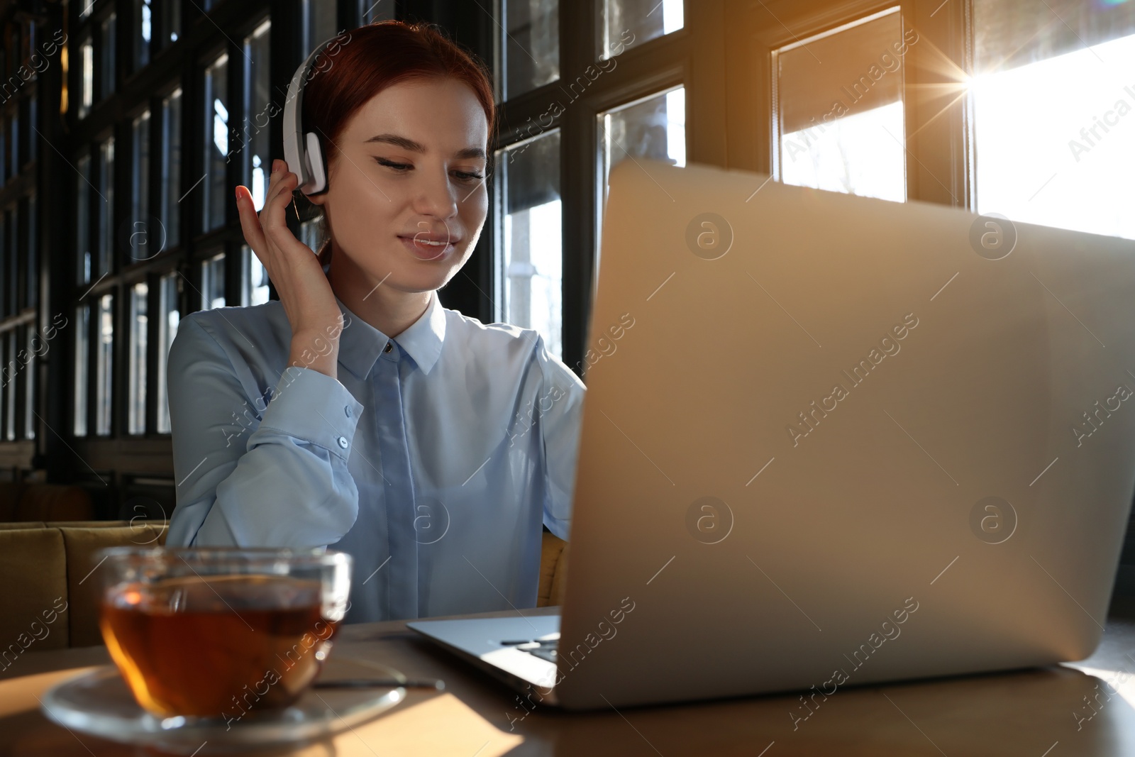 Photo of Young female student with laptop and headphones studying at table in cafe