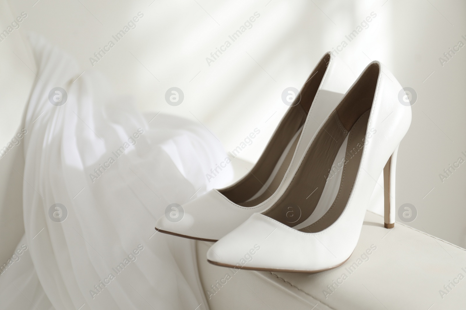 Photo of Classic white wedding shoes on sofa indoors