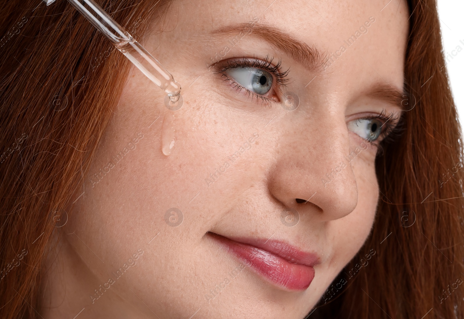 Photo of Beautiful woman with freckles applying cosmetic serum onto her face, closeup