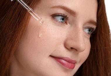 Photo of Beautiful woman with freckles applying cosmetic serum onto her face, closeup