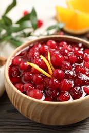Photo of Fresh cranberry sauce with orange peel on wooden table, closeup