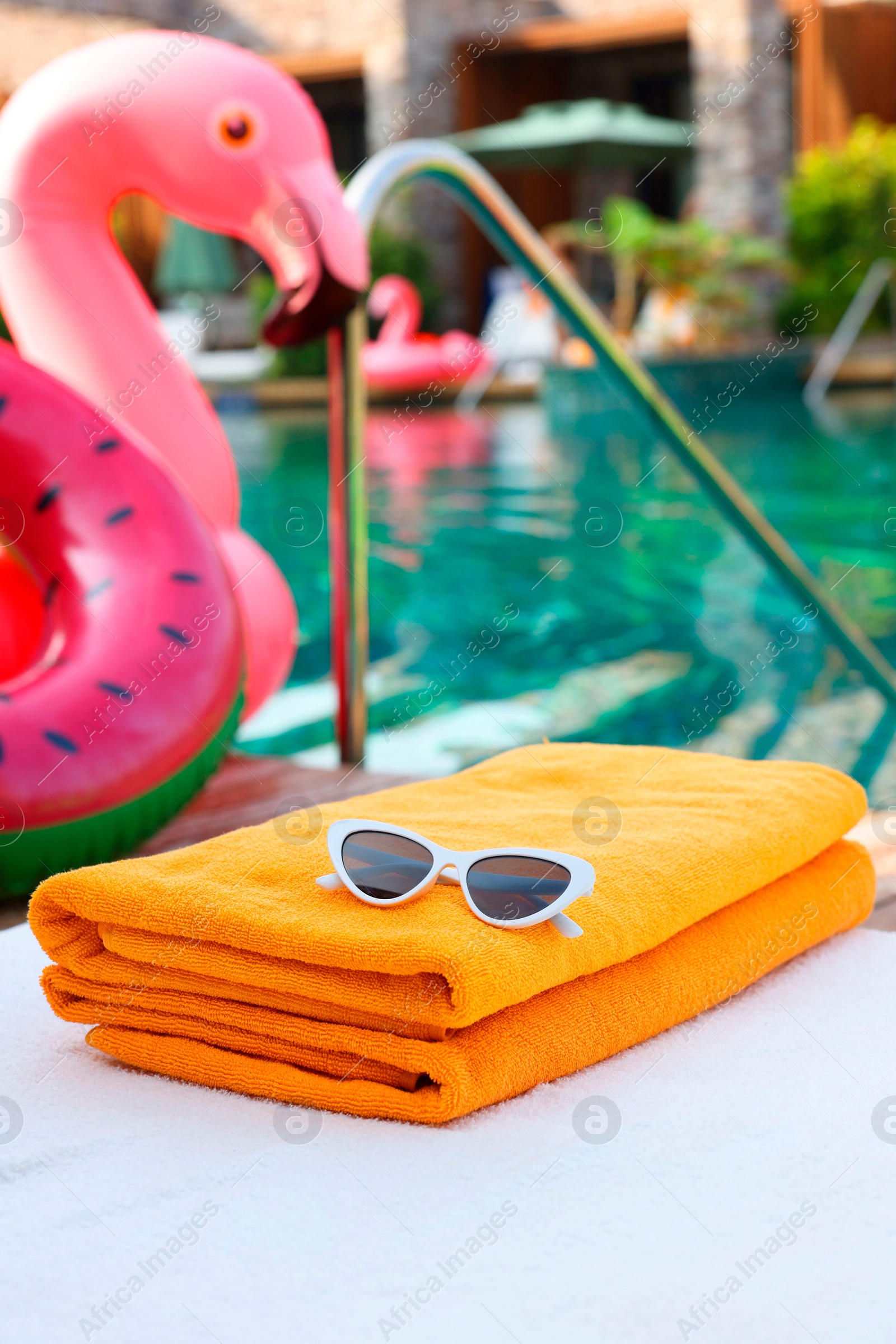Photo of Beach towels and sunglasses on sun lounger near outdoor swimming pool. Luxury resort