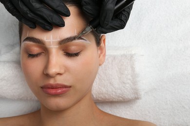 Photo of Beautician making permanent eyebrow makeup to young woman, top view. Space for text