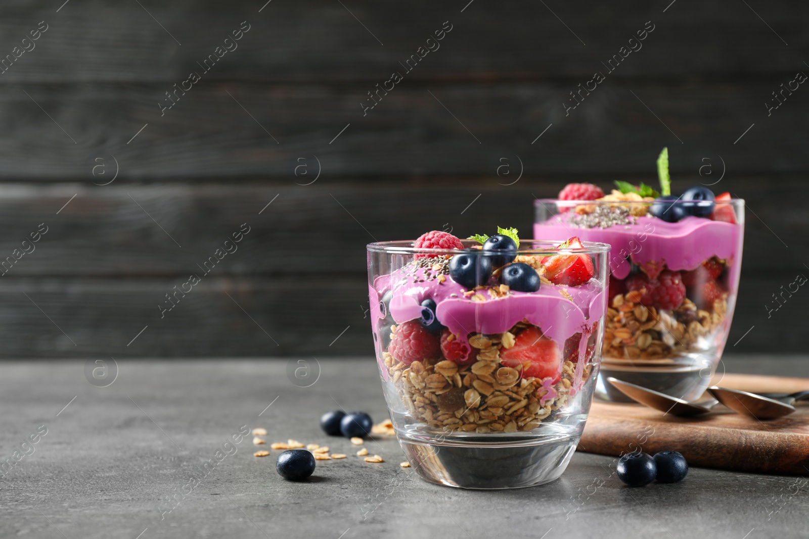 Image of Tasty dessert with acai smoothie, granola and berries on grey table. Space for text