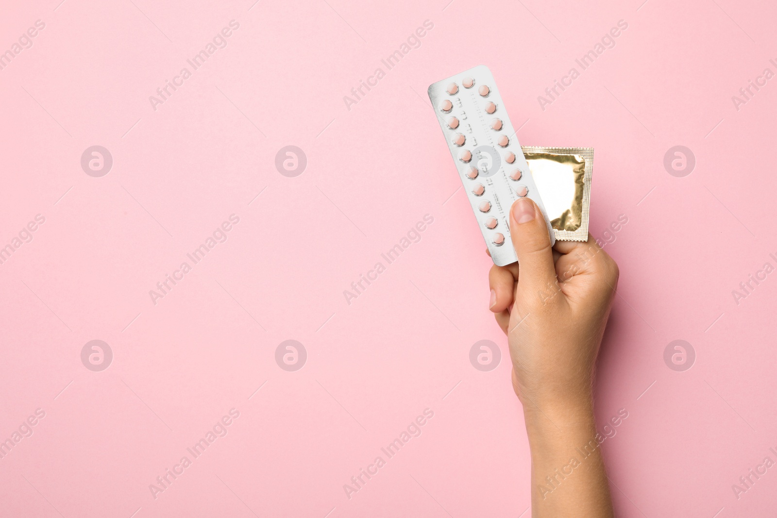 Photo of Woman holding condom and birth control pills on pink background, top view with space for text. Safe sex