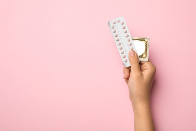 Photo of Woman holding condom and birth control pills on pink background, top view with space for text. Safe sex