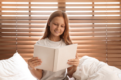 Photo of Cute preteen girl reading book on bed near window