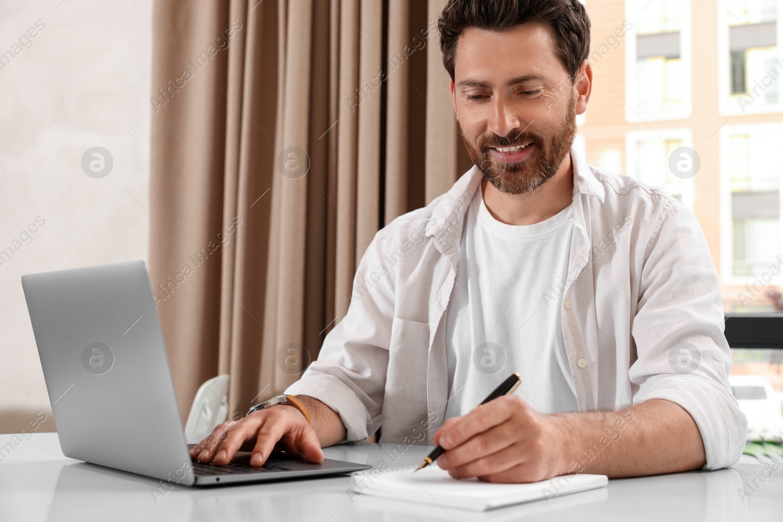 Photo of Man working on laptop and writing something at table in cafe