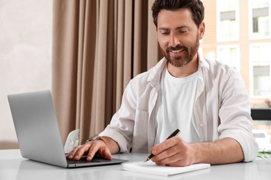 Photo of Man working on laptop and writing something at table in cafe