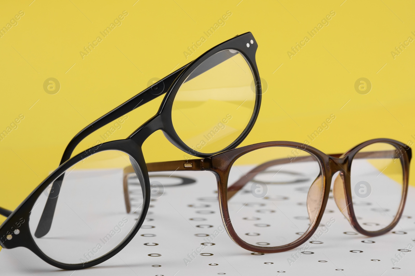 Photo of Vision test chart and glasses on yellow background, closeup