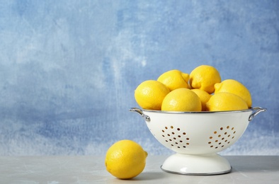 Photo of Colander with ripe lemons on table against color background