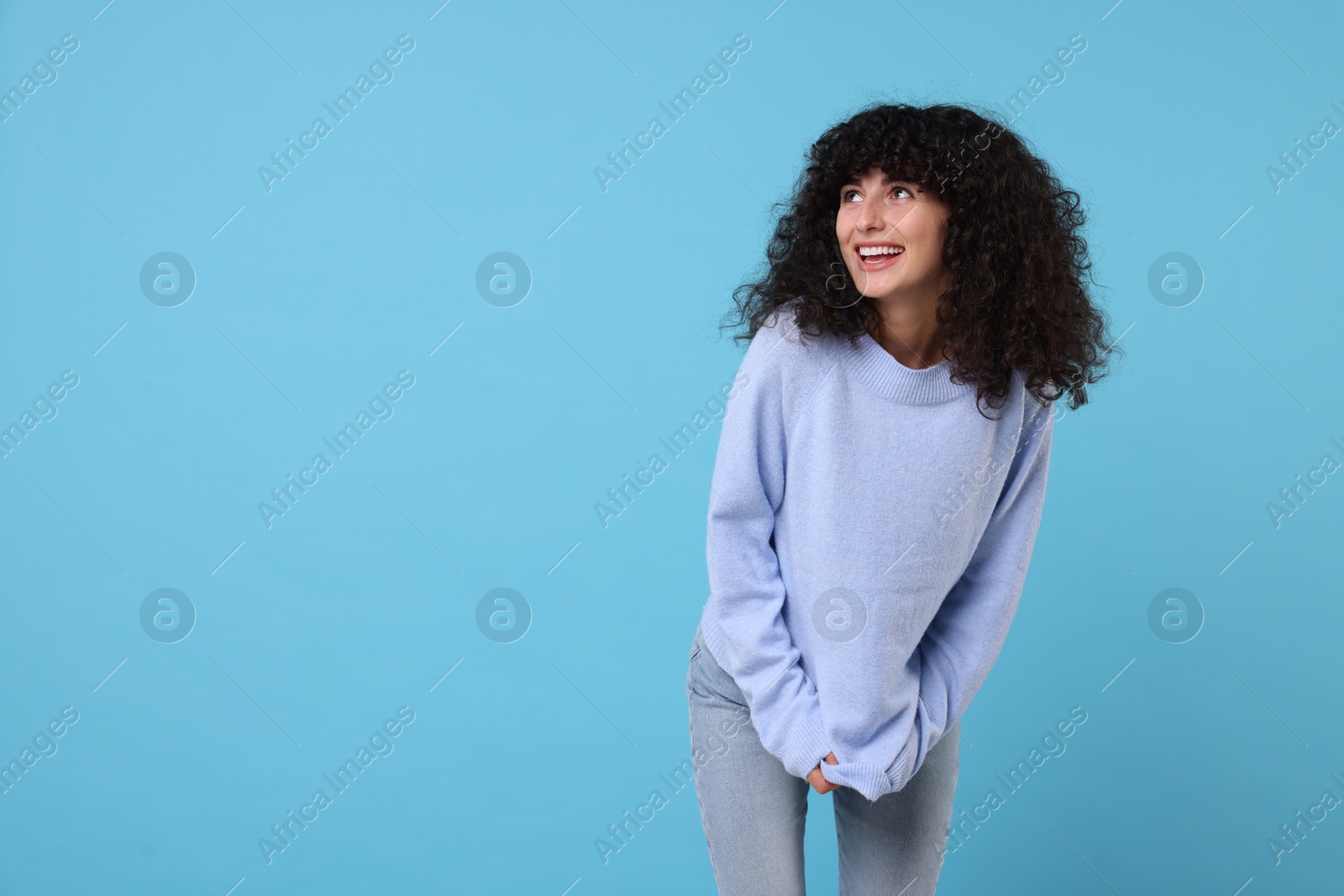 Photo of Happy young woman in stylish warm sweater on light blue background, space for text