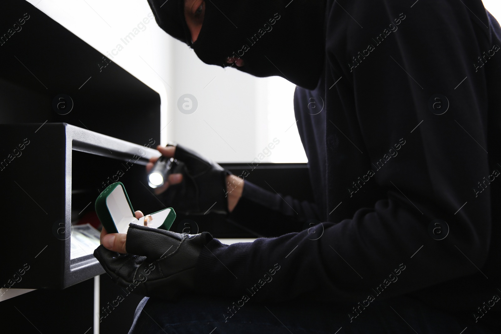 Photo of Thief taking golden ring out of steel safe indoors, closeup