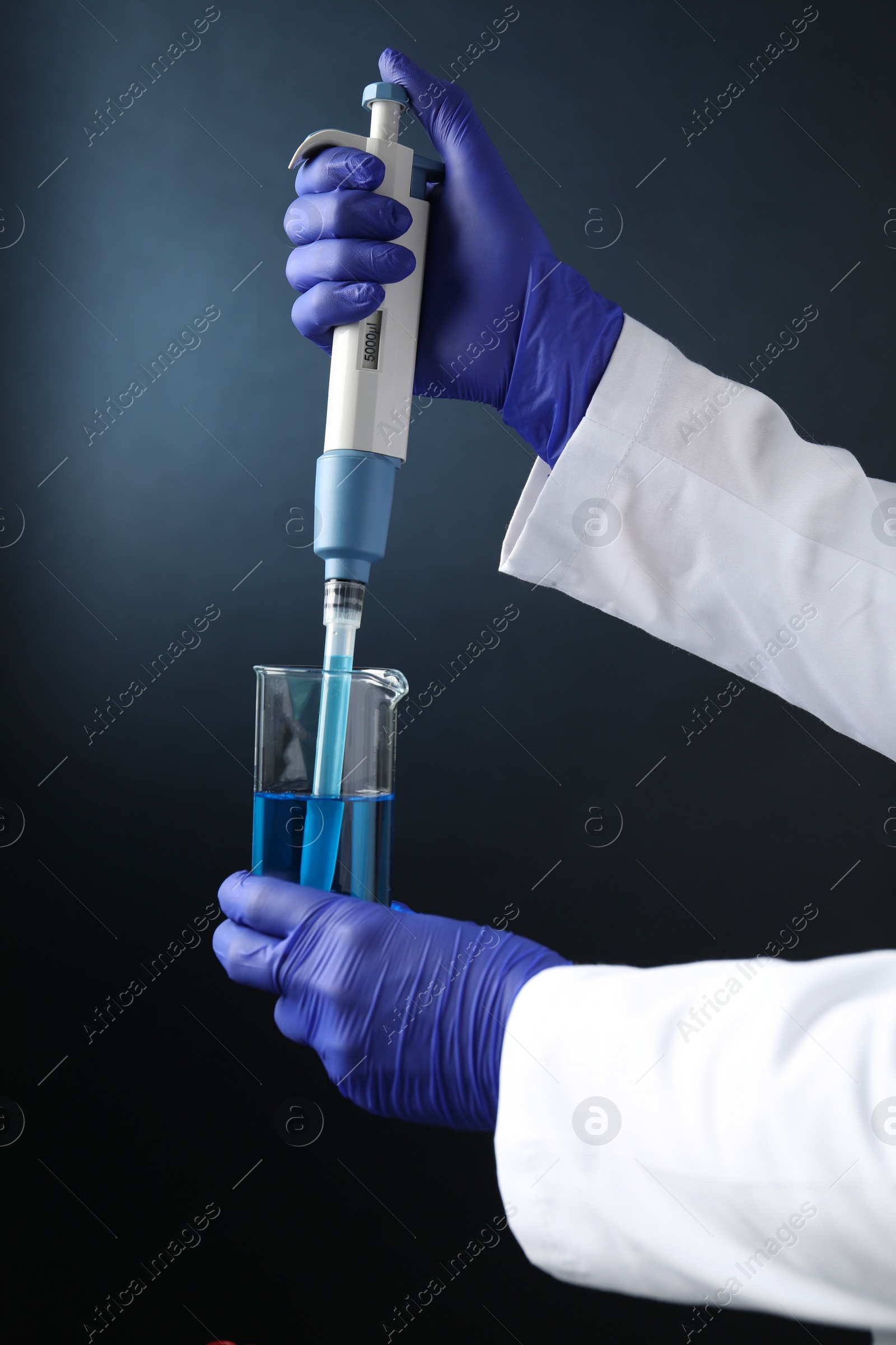 Photo of Laboratory analysis. Scientist dripping sample with micropipette into beaker on dark background, closeup