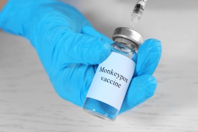 Photo of Nurse filling syringe with monkeypox vaccine from vial at white wooden table, closeup