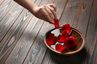 Woman with bowl of aroma spa water and rose petals on wooden background, closeup. Space for text