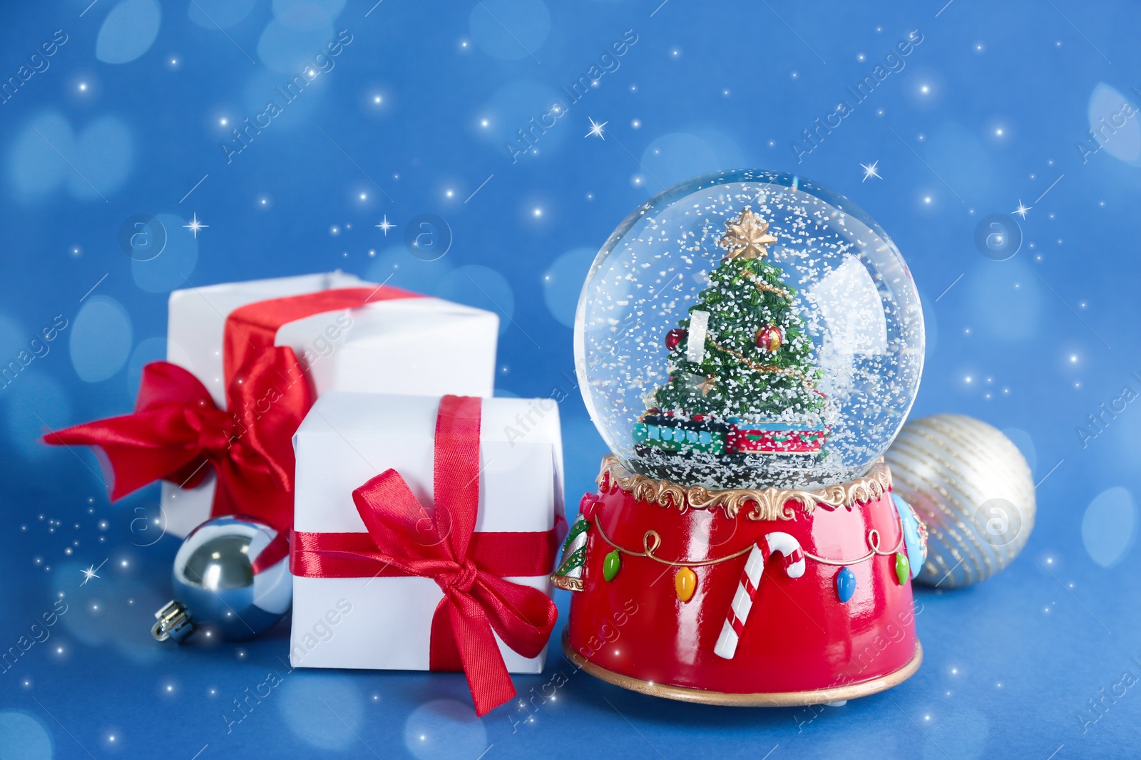 Image of Beautiful snow globe, gift boxes and Christmas balls on blue background. Bokeh effect