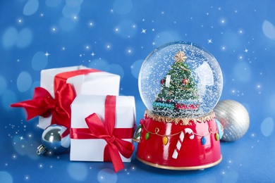 Image of Beautiful snow globe, gift boxes and Christmas balls on blue background. Bokeh effect