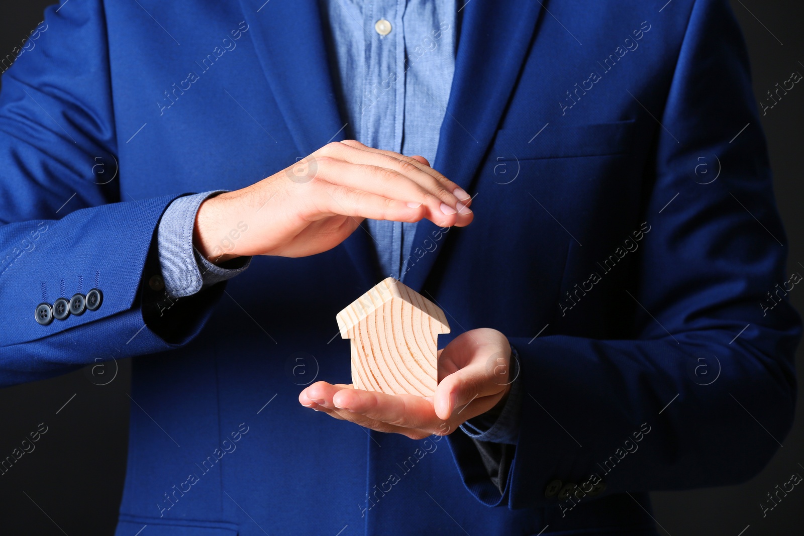 Photo of Male agent covering wooden house on black background, closeup. Home insurance