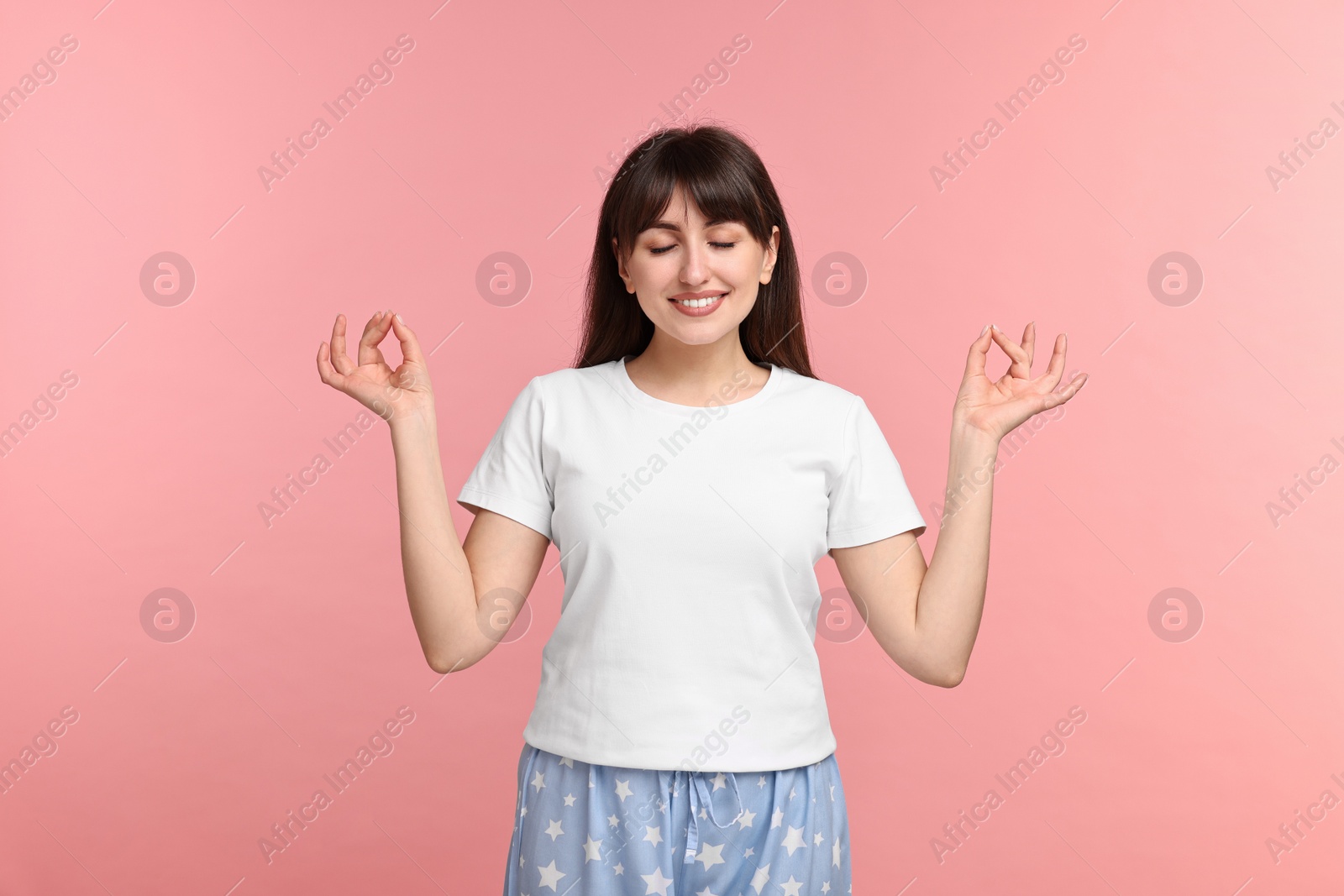 Photo of Woman in pyjama meditating on pink background