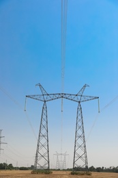 Photo of High voltage towers with electricity transmission power lines in field on sunny day
