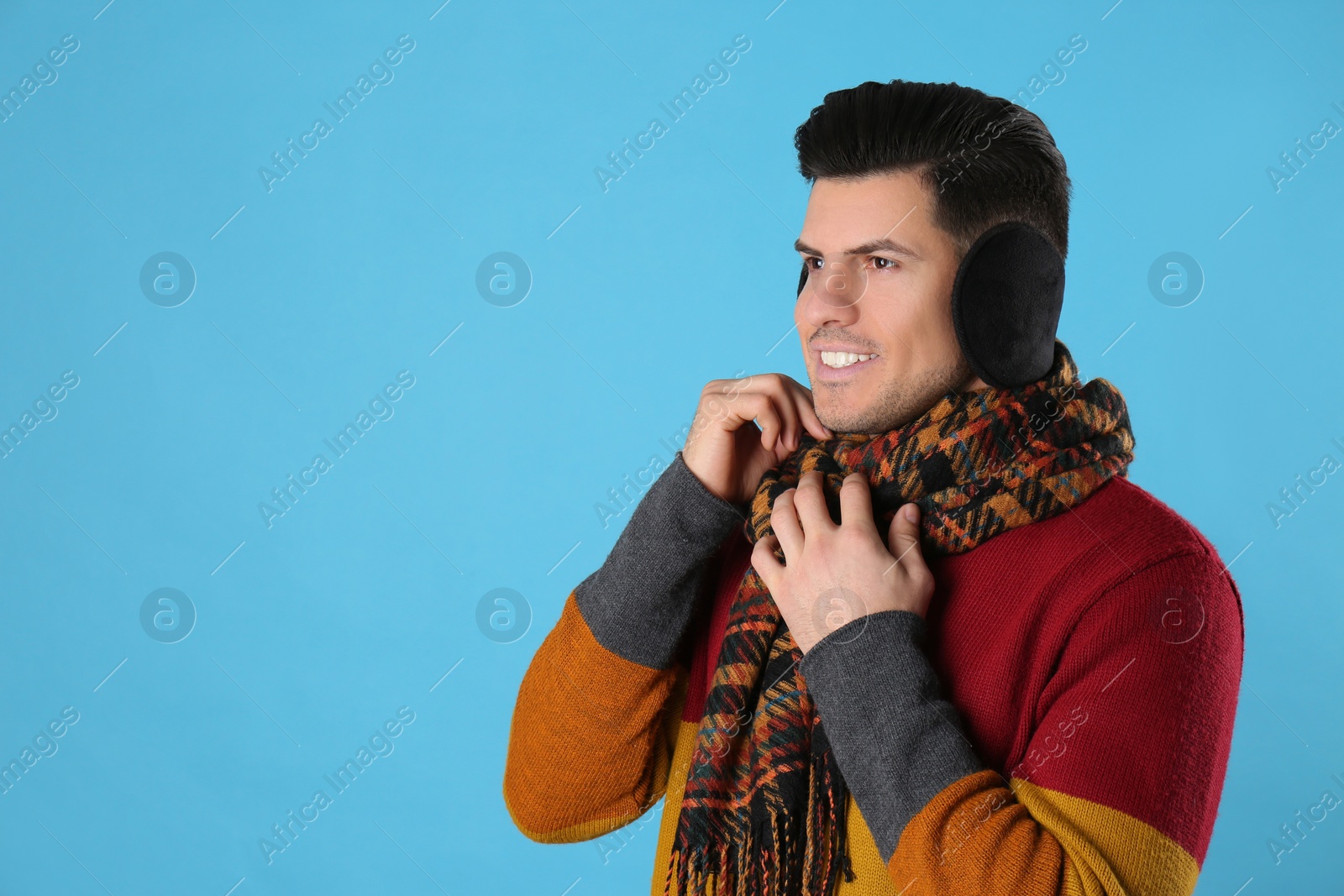 Photo of Man wearing stylish earmuffs and scarf on light blue background. Space for text