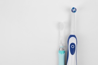 Photo of Electric toothbrushes on white background, flat lay. Space for text