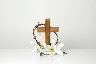 Photo of Wooden cross, crown of thorns and blossom lilies on table against light background