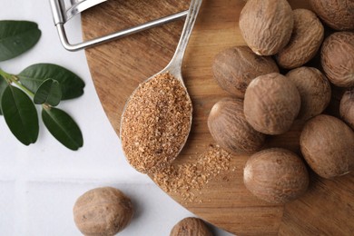 Spoon with grated nutmeg, seeds and green branch on white table, flat lay