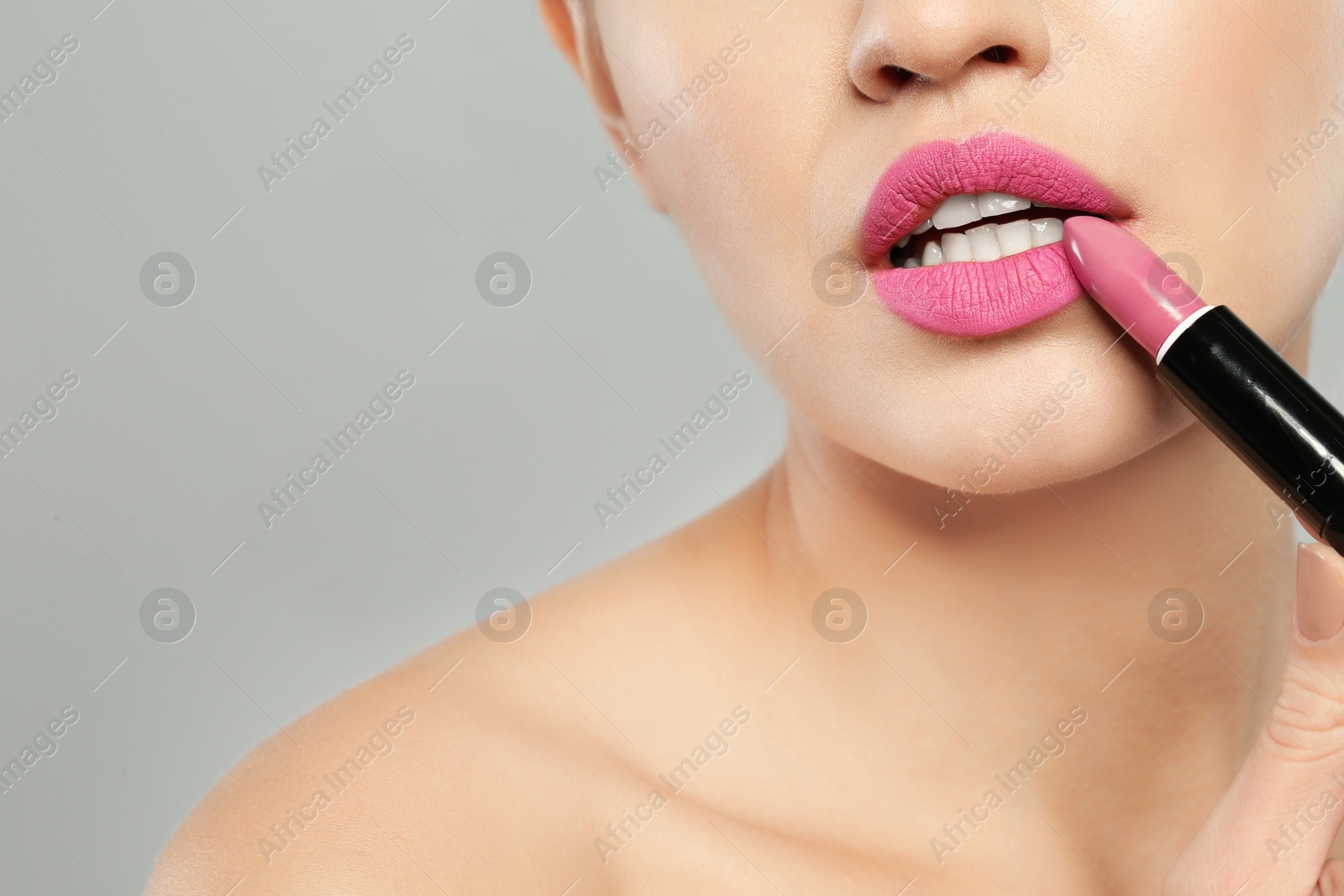 Photo of Young woman applying beautiful lipstick on gray background, closeup. Space for text