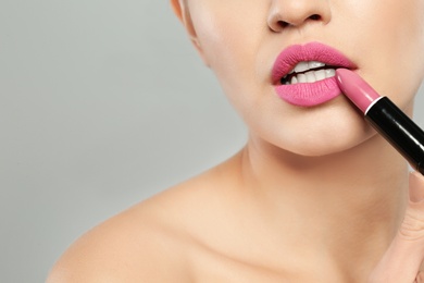 Young woman applying beautiful lipstick on gray background, closeup. Space for text