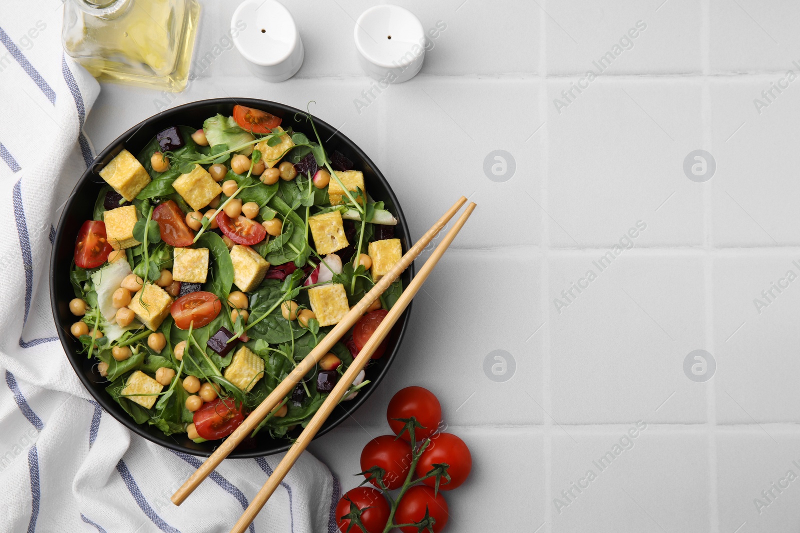 Photo of Tasty salad with tofu, chickpeas and vegetables served on white tiled table, flat lay. Space for text