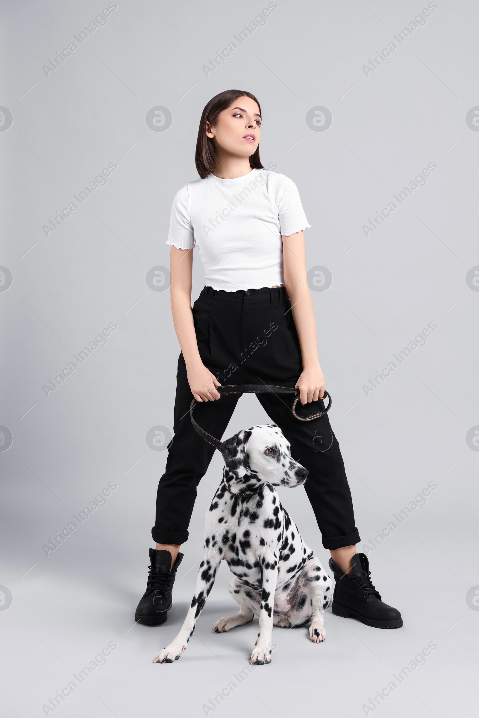 Photo of Beautiful young woman with her adorable Dalmatian dog on light grey background. Lovely pet