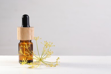 Photo of Bottle of essential oil and fresh dill on white table, space for text