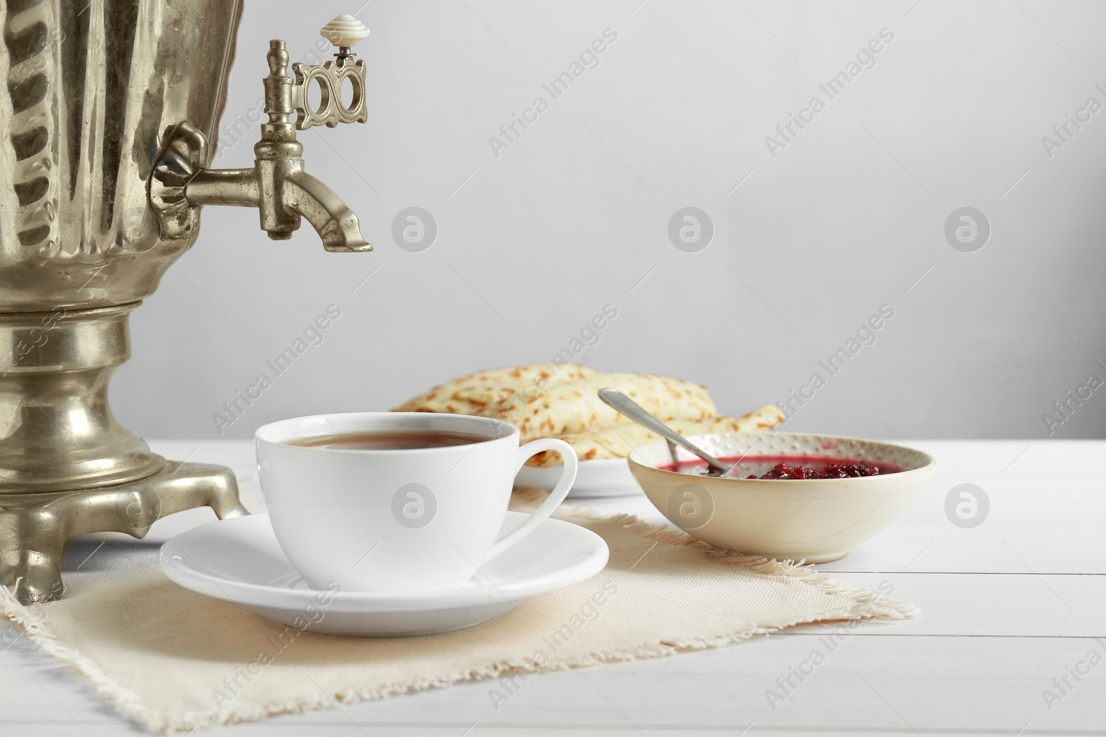 Photo of Vintage samovar, cup of hot drink and snacks served on white wooden table. Traditional Russian tea ceremony