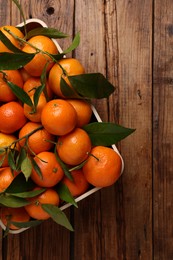 Photo of Fresh tangerines with green leaves in crate on wooden table, top view