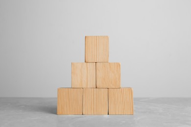 Pyramid of blank wooden cubes on grey table against light background. Space for text
