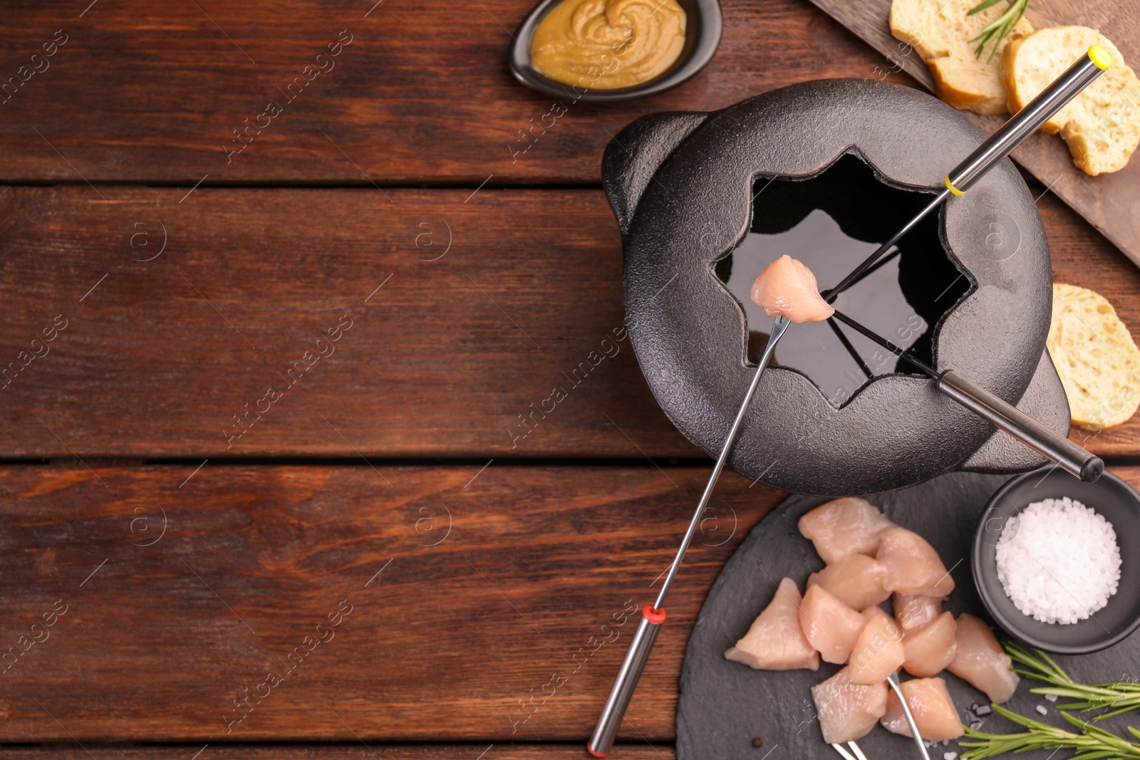 Photo of Fondue pot, forks, pieces of raw meat, bread and spices on wooden table, flat lay. Space for text