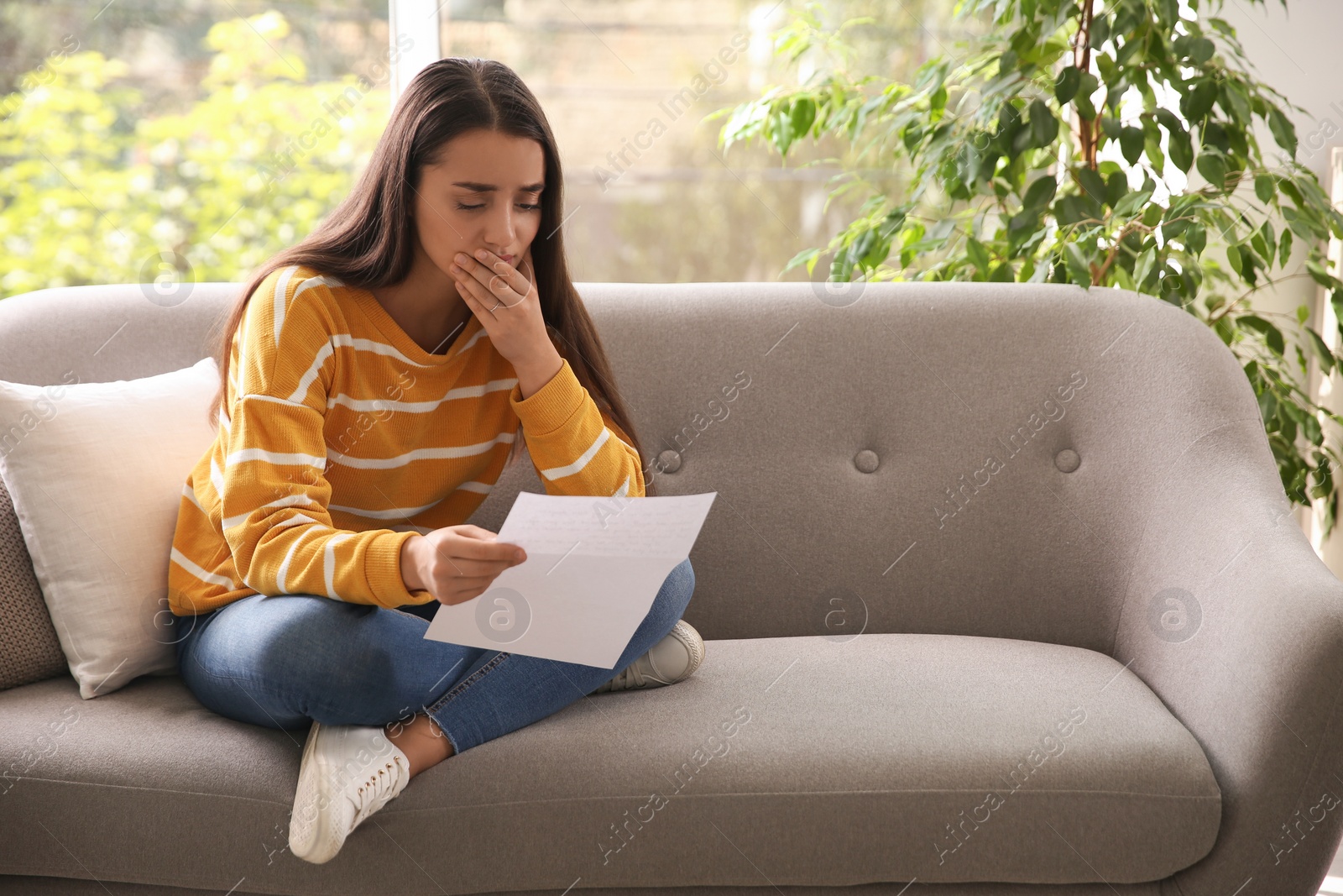 Photo of Worried woman reading letter on sofa at home