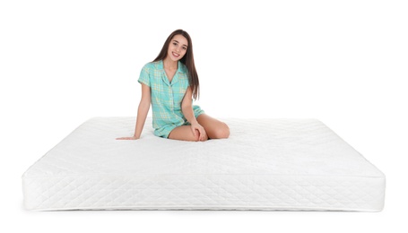 Young woman sitting on mattress against white background