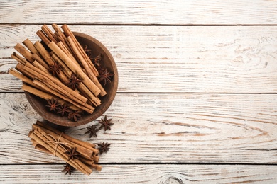 Photo of Aromatic cinnamon sticks and anise on white wooden table, flat lay. Space for text