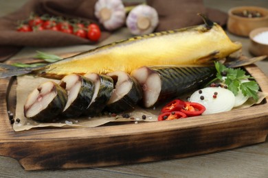 Delicious smoked mackerels with pepper, onion and spices on wooden table, closeup