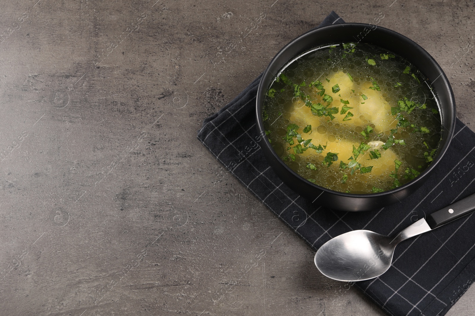 Photo of Delicious chicken soup with parsley and spoon on grey table, above view. Space for text