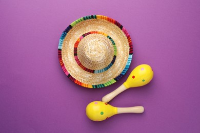 Photo of Mexican sombrero hat and maracas on purple background, flat lay