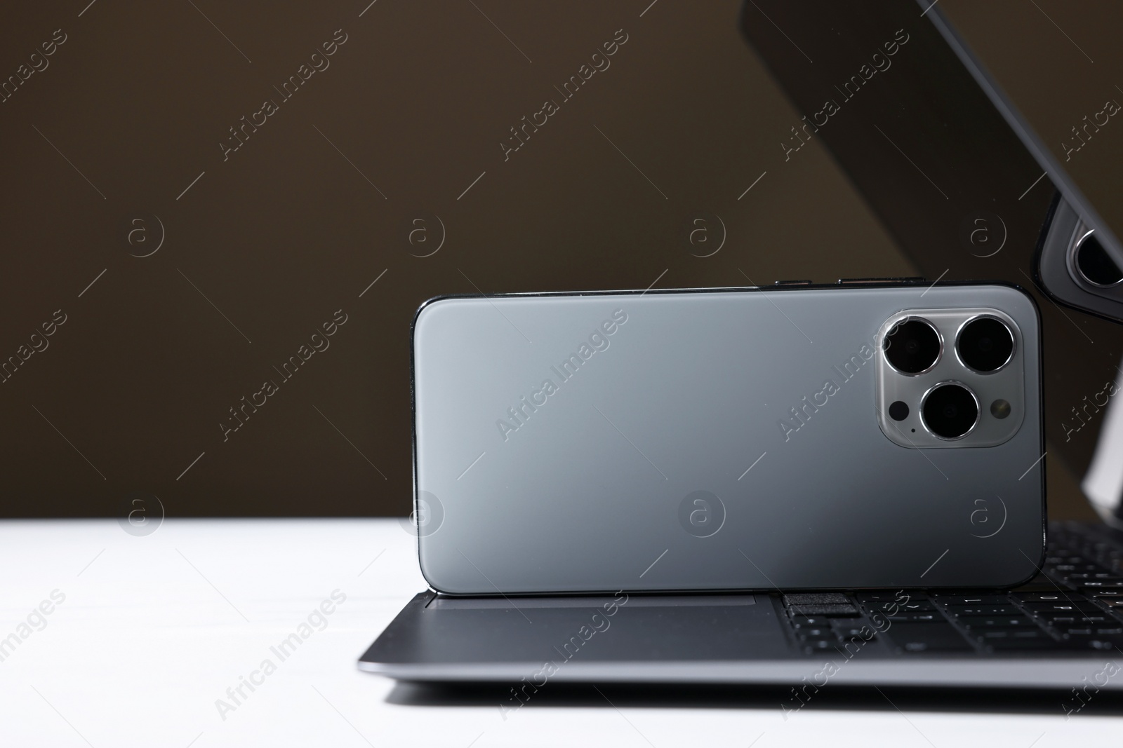 Photo of Modern laptop and smartphones on white table against brown background. Space for text