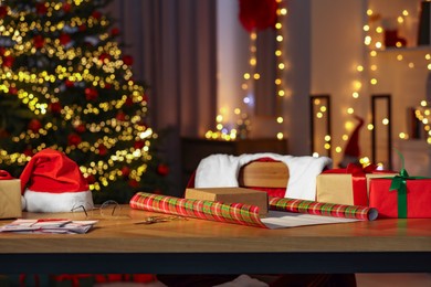 Santa's Claus workplace. Gift boxes, wrapping paper, letters on table and costume in room with Christmas tree