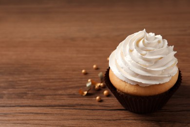 Photo of Delicious cupcake decorated with cream on wooden table, space for text