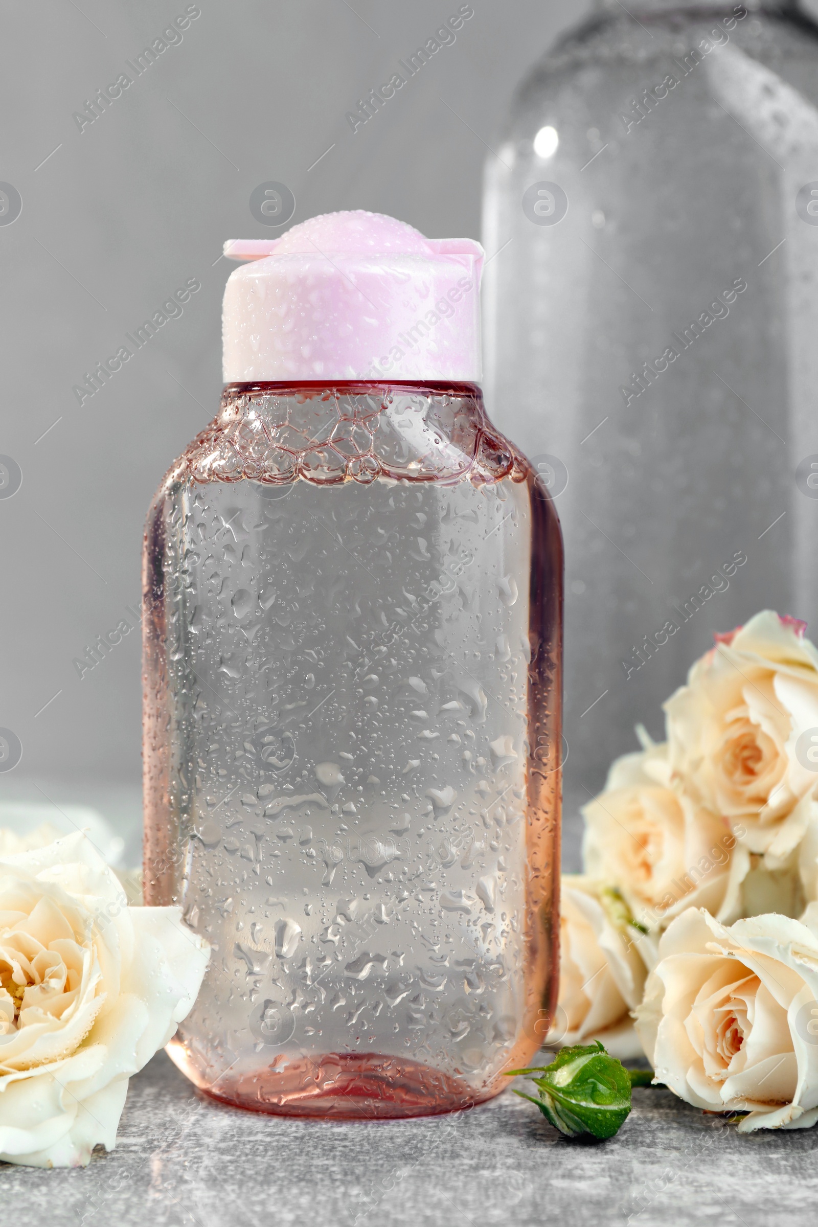 Photo of Micellar water and roses on grey table, closeup